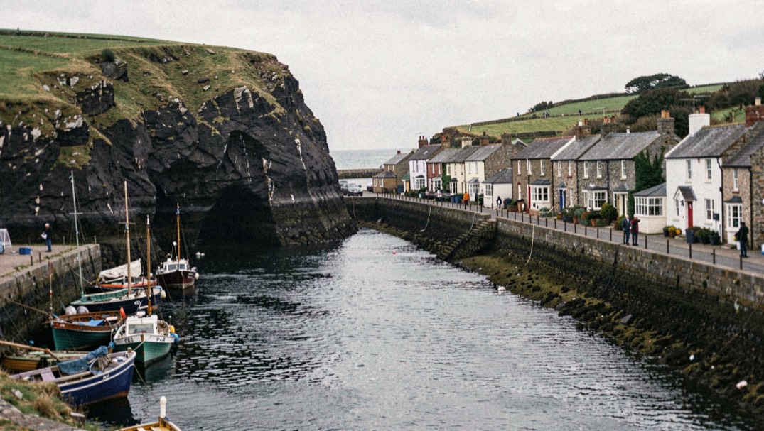 Narrow harbour mouth at Staithes with cobles moored below a dark headland and tightly packed cottages along the beck